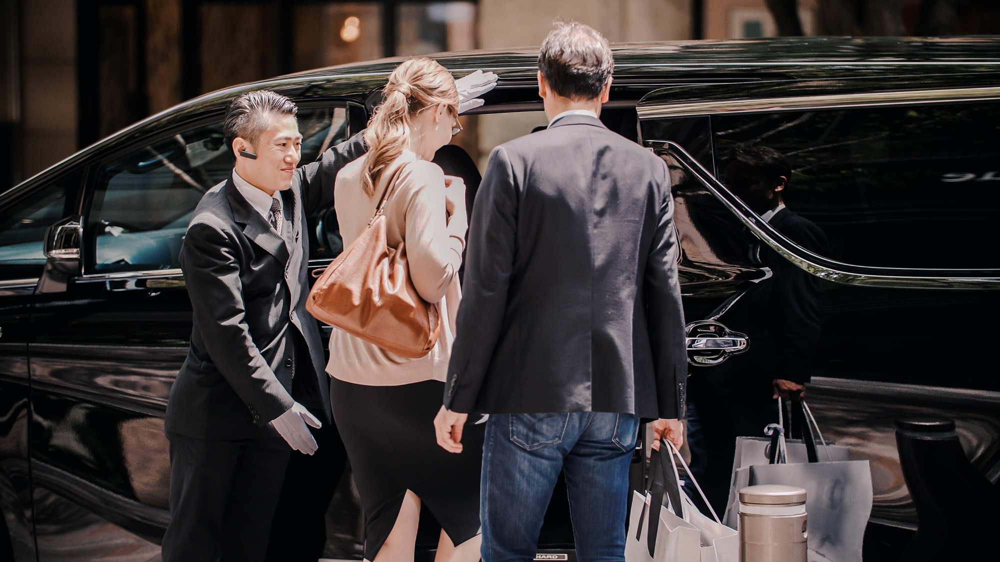 Chauffeur in an immaculate suit welcoming guests into a luxury vehicle at the airport terminal
